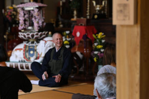 慶學寺に集まった多くの様々な年齢の方々へやさしく身振り手振りで坐禅の説明を解説するGarvey住職のようす。
