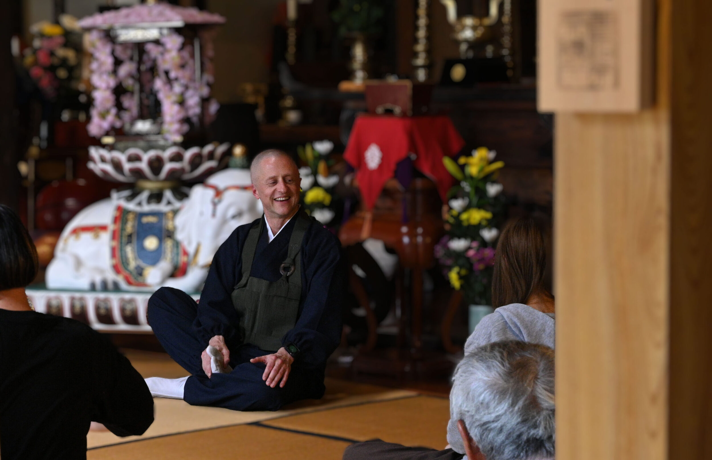 慶學寺に集まった多くの様々な年齢の方々へやさしく身振り手振りで坐禅の説明を解説するGarvey住職のようす。
